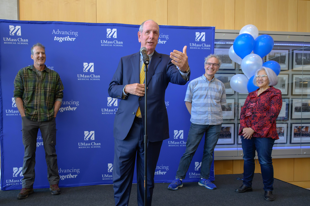 Chancellor Collins speaking at a campus Nobel celebration in October. He shares the stage with Craig Mello, Victor Ambros and Rosalind Lee. Their is a UMass Chan banner in the background and Collins is speaking into a microphone. 