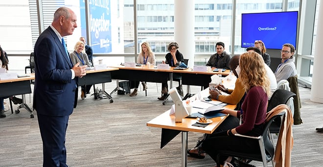 Chancellor Collins wearing a suit speaking in front of participants