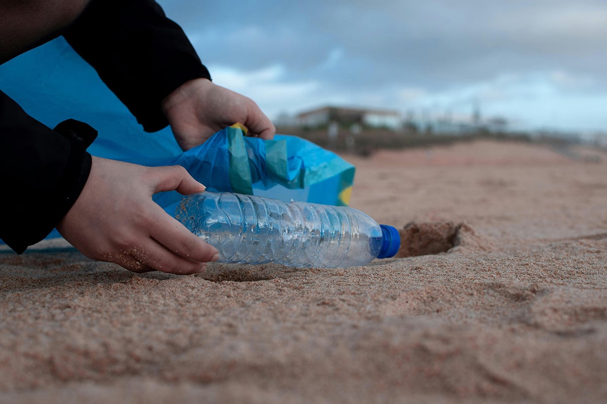 hand picking up water bottle trash on the beach