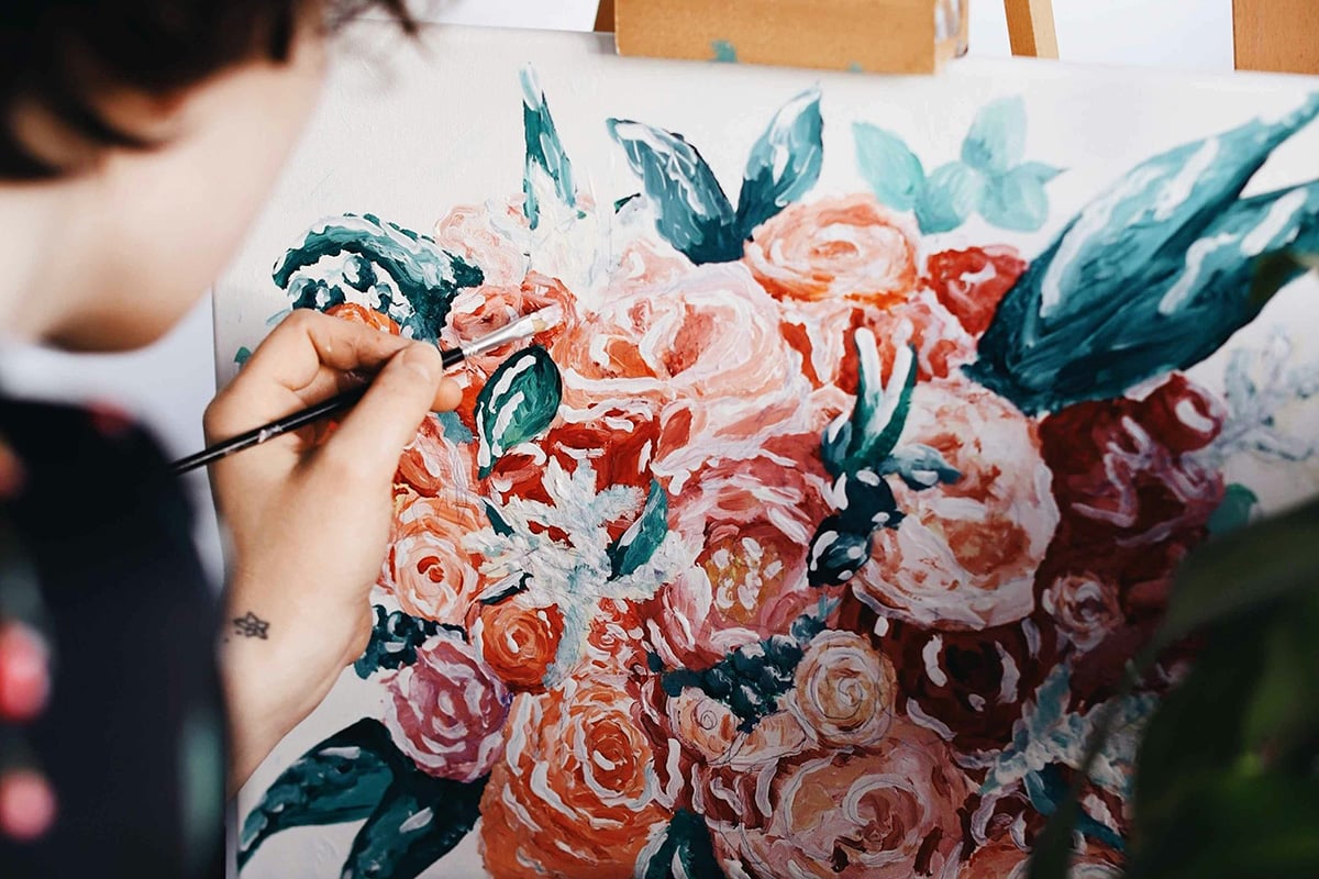 person painting flowers on a canvas